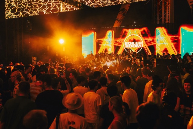 A dense crowd dancing by a stage in orange light