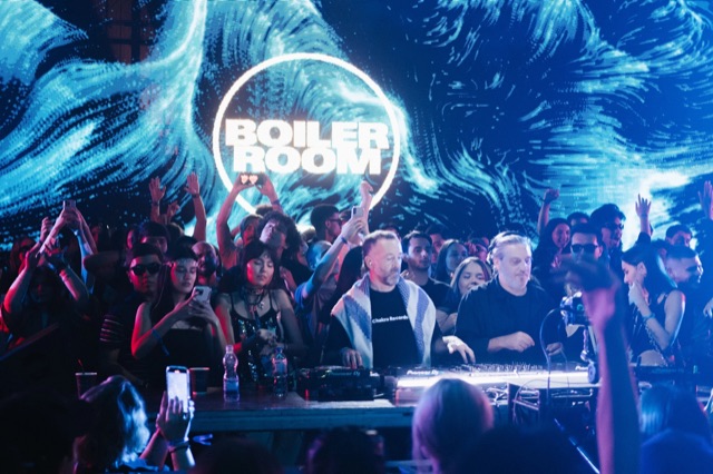 DJs performing against a blue Boiler Room stage