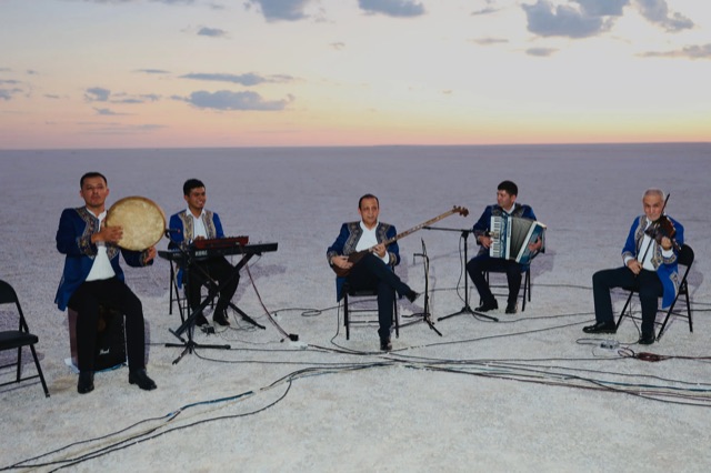 An ensemble performing on an open plain at sunset